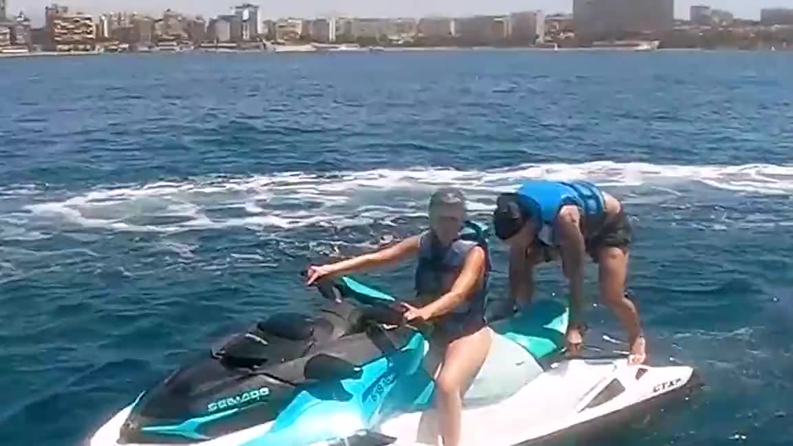 Moto de agua con dos pasajeros navegando frente al skyline de Alicante